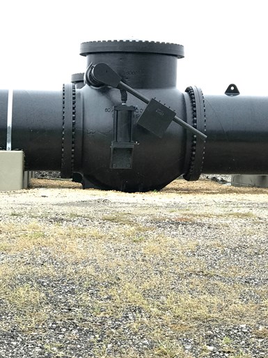 Photo of large, 60-inch check valve installed in pipeline with grass and gravel field in background
