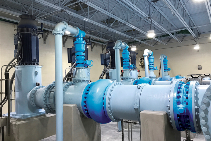 Photo of pump house with five gray and blue painted pumps with pipe and valves in place.