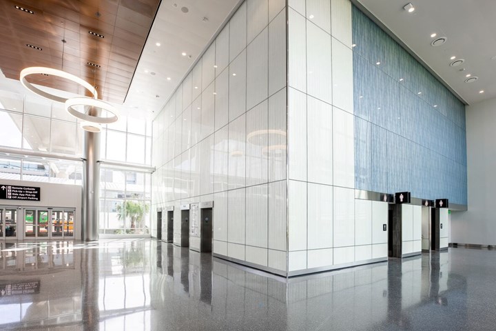 Photo of building lobby with glossy white lacquered wall panels, a wood paneled ceiling and contemporary round lights.