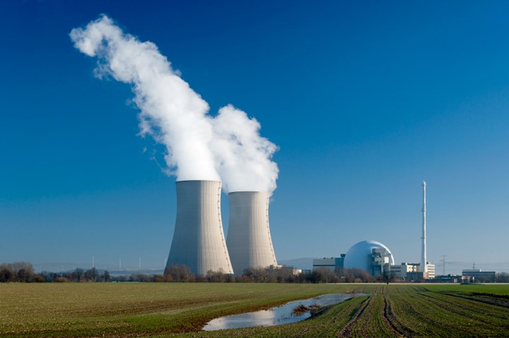 Photo of two cooling towers emitting steam and nuclear reactor building set against blue sky