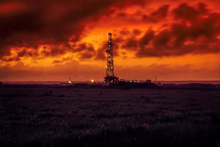 Photo of oil right with bright orange and red sunset behind it with clouds in sky