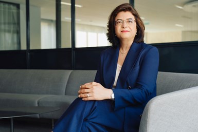 Photo of ArcVera Renewables CEO Hinda Gharbi in blue pantsuit sitting on gray couch in office setting